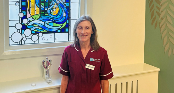 Barbara photographed in a burgundy work tunic in front of a blue stained glass window