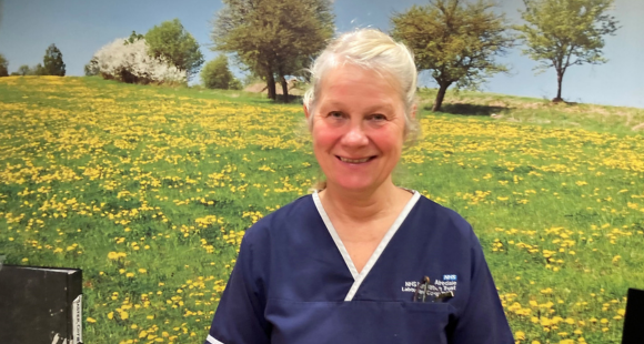 Bev photographed in her dark blue work tunic in front of a wall mural showing a green hillside