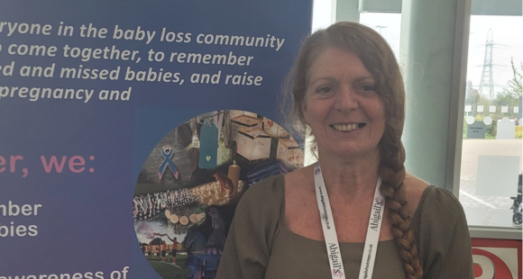Sharon Hurst photographed stood next to a purple banner about baby loss