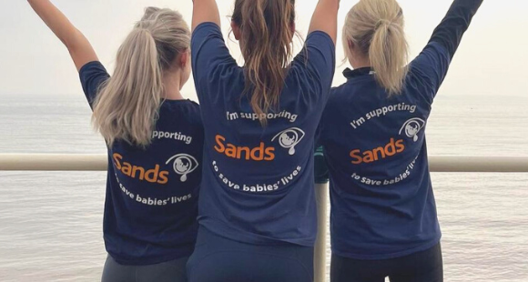 photo of three women with their backs to the camera with their arms in the air wearing Sands t-shirts