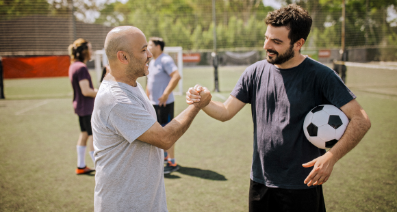 Two men stood together and joining hands with one of them holding a ball