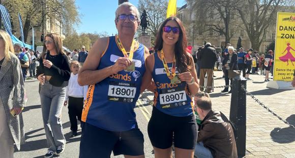 One man and one woman runners wearing Sands running vests posing for a photo holding their race medal.