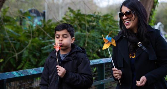 Woman and young boy walking along in Sands hoodie blowing windmills