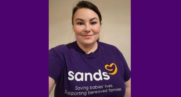 A lady with dark hair smiling at the camera wearing a purple Sands saving babies live t-shirt