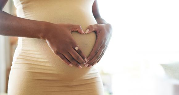 A pregnant woman holding her hands in a heart shape on her pregnancy bump.