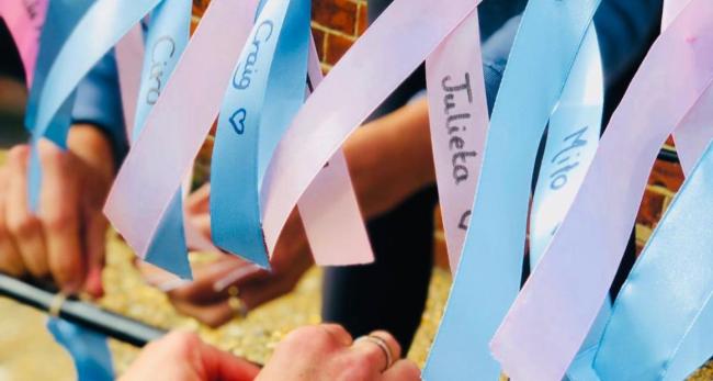 Hands tying pink and blue ribbons with babies' names