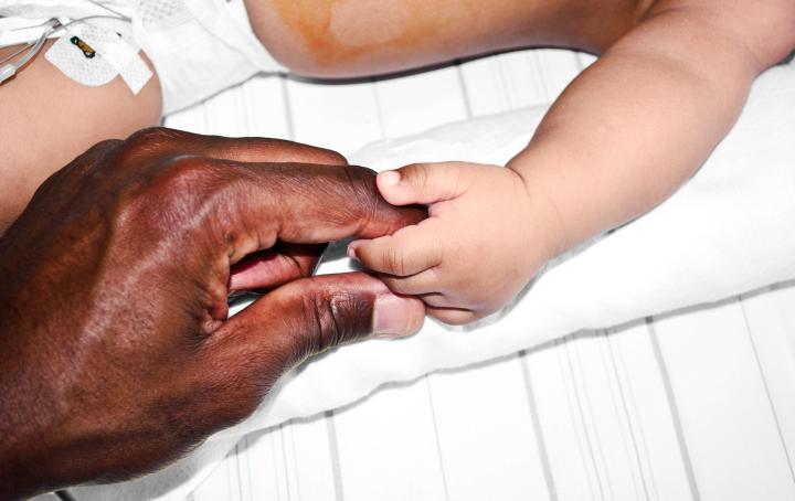 A parent's hand is holding a baby's finger