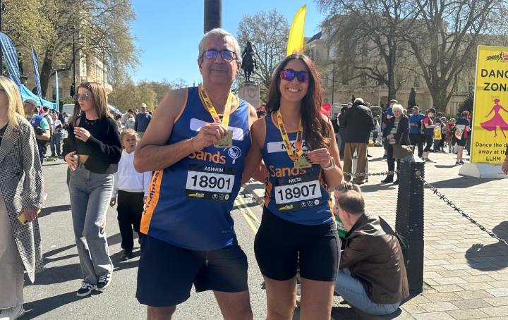 One man and one woman runners wearing Sands running vests posing for a photo holding their race medal.