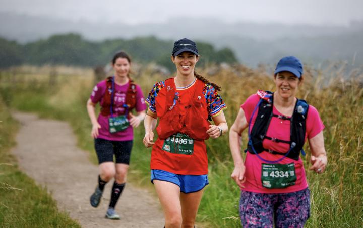 Three women running on a path with long grass in background
