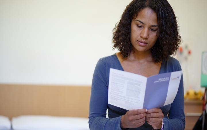 A woman with dark hair looks at a leaflet in her hand