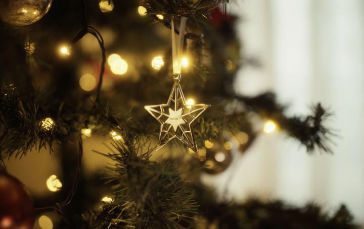 A golden star christmas tree decoration with Sands logo hangs on a beautifully lit Christmas tree.