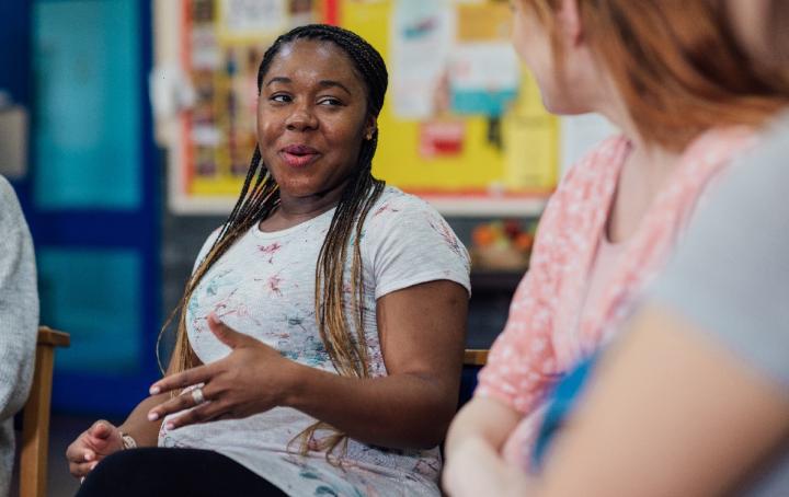 Two women sit in conversation, only one can be seen front on, the other is seen from a side angle